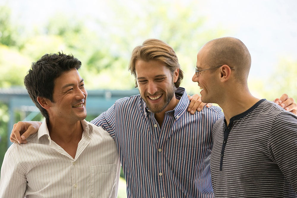 Three men smilling and giving each other side hugs