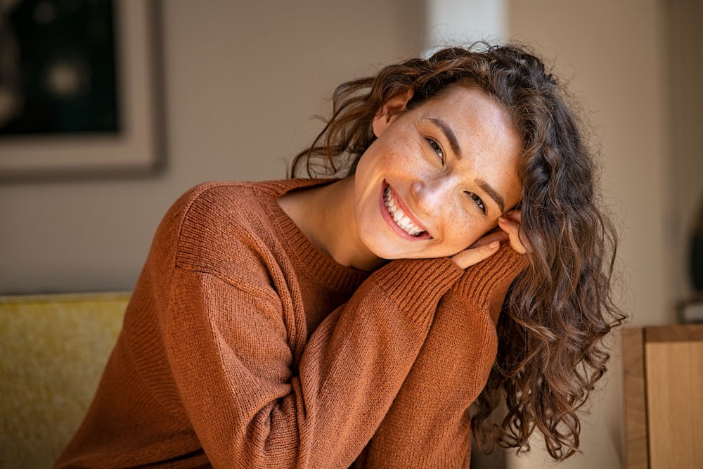 Smiling young woman rests her head sideways on her hands during Dual Diagnosis Treatment