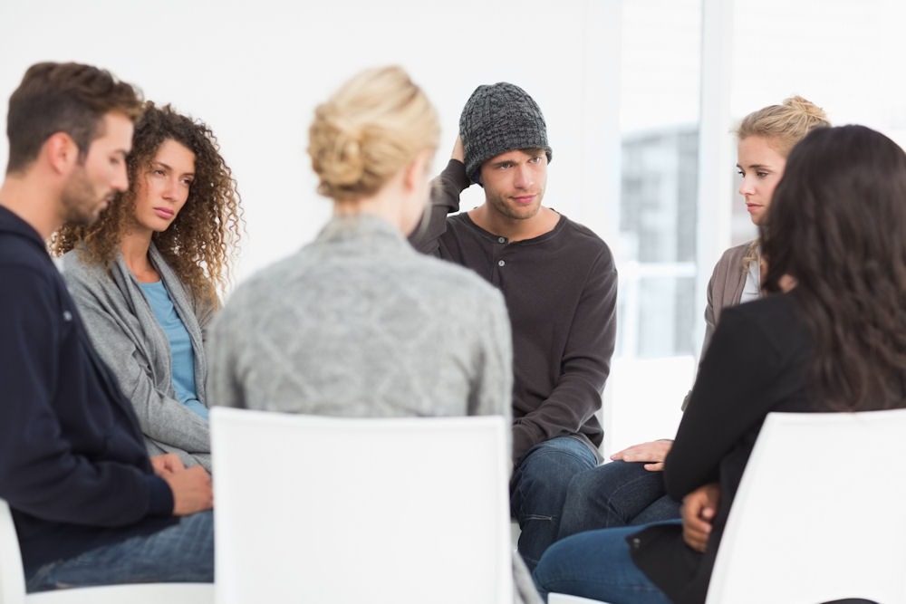 php-addiction-therapy Young man shifts uncomfortably while speaking in group therapy