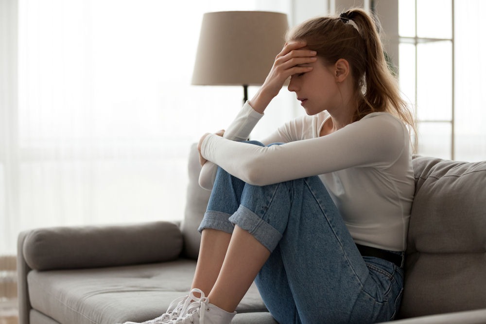 benzodiazepine-addiction-treatment-center Young woman sitting on couch, feeling distressed and considering benzodiazepine addiction treatment