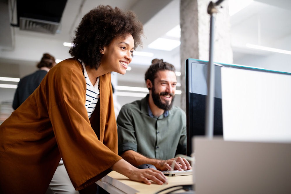 bipolar-and-addiction-treatment Woman leaning down to read computer monitor while man types on attached keyboard.
