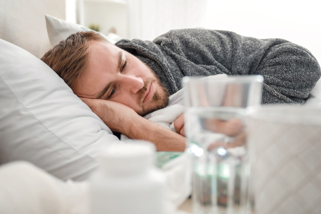Man with PAWS laying in bed with medication and water on the nearby nightstand.