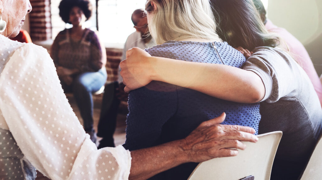 Women of different ages hugging each other while sitting at a rehab facility.