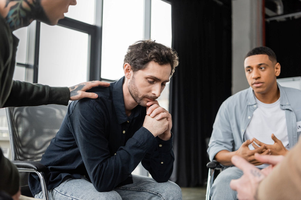 People consoling man speaking in a support group for cocaine addiction
