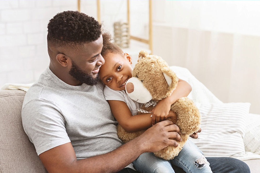 Man holding daughter with teddy bear after undergoing individual therapy for addiction