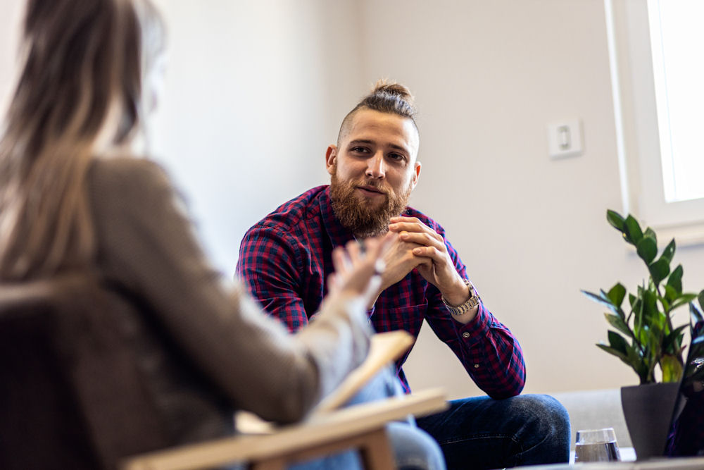 Smiling man with bun sits in group therapy for heroin addiction.
